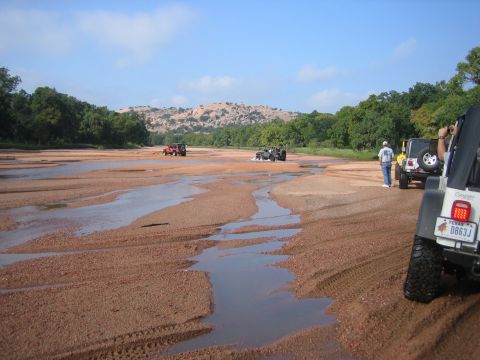 2001 Jeep Wrangler - Jeeps traverse a dry riverbed under a clear blue sky, with rocky hills in the distance.