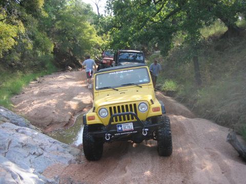 2001 Jeep Wrangler - A yellow 2001 Jeep Wrangler navigates a challenging off-road trail with other vehicles following.
