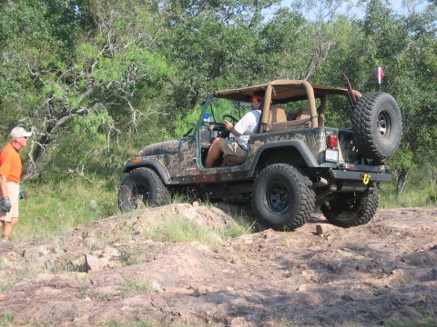 2001 Jeep Wrangler - A driver navigates a Jeep Wrangler over a rough, rocky terrain with trees in the background.