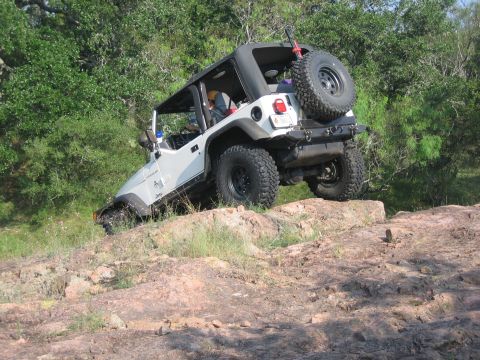 2001 Jeep Wrangler - A white Jeep Wrangler navigates a rocky trail with trees in the background.