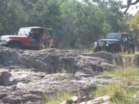 2001 Jeep Wrangler - Two Jeep Wranglers tackle a challenging rocky off-road course amidst trees and dry grass.