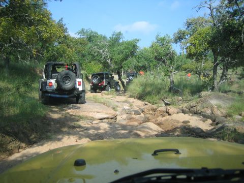 2001 Jeep Wrangler - A convoy of Jeeps navigates a challenging off-road trail surrounded by trees and large rocks.