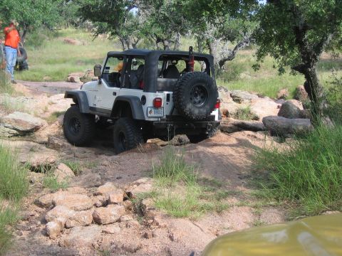 2001 Jeep Wrangler - A white Jeep Wrangler tackles a challenging off-road course with rocky terrain and sparse trees.