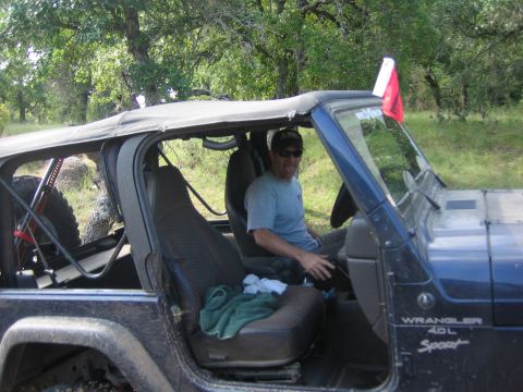2001 Jeep Wrangler - A man sits in a blue 2001 Jeep Wrangler with the doors off and a red flag attached to the windshield.