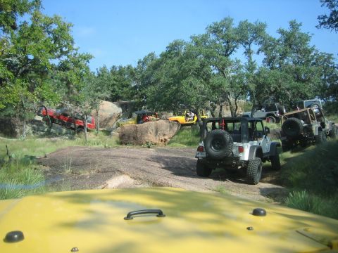 2001 Jeep Wrangler - Multiple Jeep Wranglers traverse a challenging off-road trail surrounded by natural rock formations and trees.