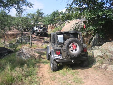 2001 Jeep Wrangler - Jeeps navigate a challenging off-road trail with large boulders and trees.
