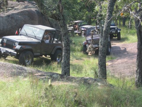 2001 Jeep Wrangler - Multiple Jeeps navigate a rough, off-road trail surrounded by trees and large rocks.