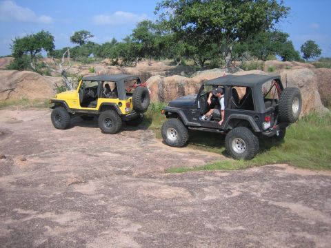 2001 Jeep Wrangler - Two Jeep Wranglers, one yellow and one black, are parked on a rocky landscape during an off-road excursion.