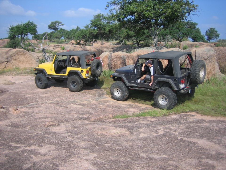 Yellow and black 2001 Jeep Wranglers parked on rocky terrain with trees and boulders in background