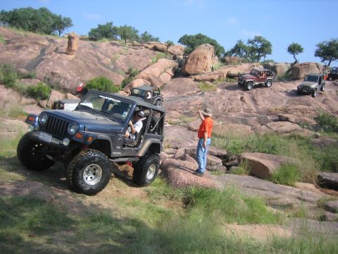 2001 Jeep Wrangler - Several Jeep Wranglers navigate a rocky, off-road trail under a clear blue sky.