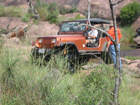2001 Jeep Wrangler - Orange Jeep Wrangler navigating a rocky, off-road trail with dense vegetation.