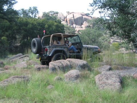 2001 Jeep Wrangler - A camouflaged 2001 Jeep Wrangler navigates a rocky, grassy landscape during an off-road excursion.
