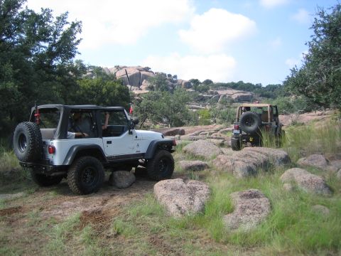 2001 Jeep Wrangler - Two Jeep Wranglers navigate a rocky, off-road trail under a partly cloudy sky.