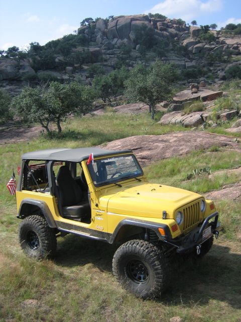 2001 Jeep Wrangler - A yellow Jeep Wrangler is parked on a grassy hill with large rock formations behind it.