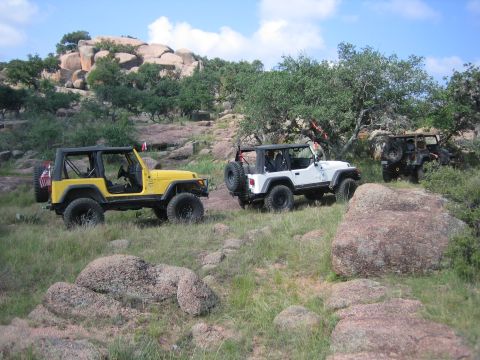 2001 Jeep Wrangler - Three Jeep Wranglers navigate a , rocky terrain under a partly cloudy sky.