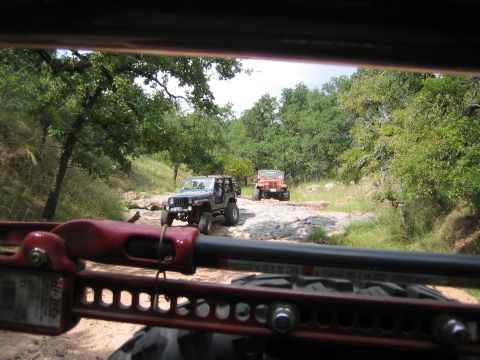 2001 Jeep Wrangler - Two Jeep Wranglers navigate a rough, rocky path through a wooded area.