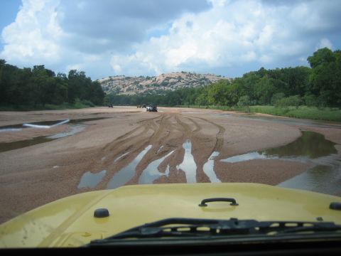 2001 Jeep Wrangler - Multiple vehicles navigate a wet, sandy terrain under a cloudy sky with a rocky hill in the distance.