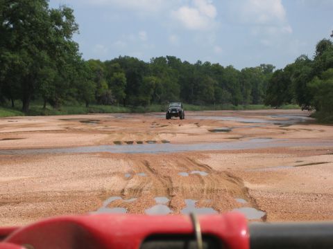 2001 Jeep Wrangler - A Jeep Wrangler navigates a dry riverbed, kicking up dust and water.