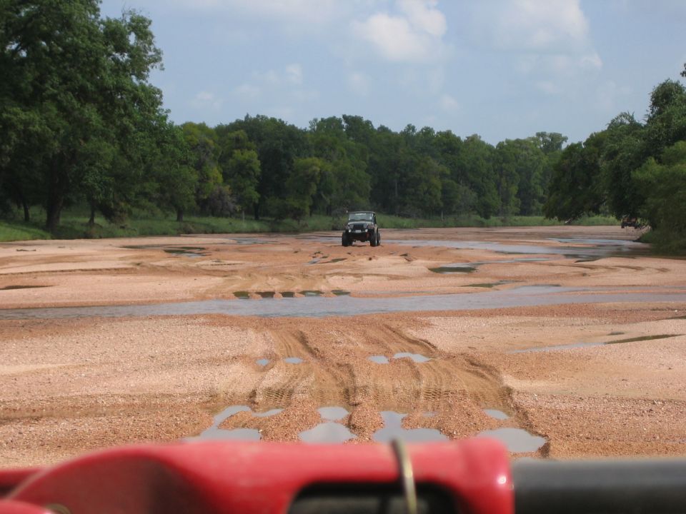 2001 Jeep Wrangler driving on a sandy, wet riverbed with trees in the background