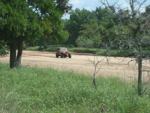 2001 Jeep Wrangler - A lone Jeep Wrangler navigates a dry riverbed surrounded by lush greenery and trees.
