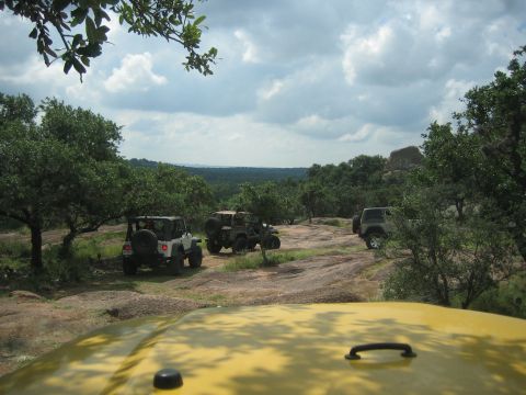 2001 Jeep Wrangler - Three Jeep Wranglers navigate a rocky, off-road trail surrounded by trees and a vast, cloudy sky.