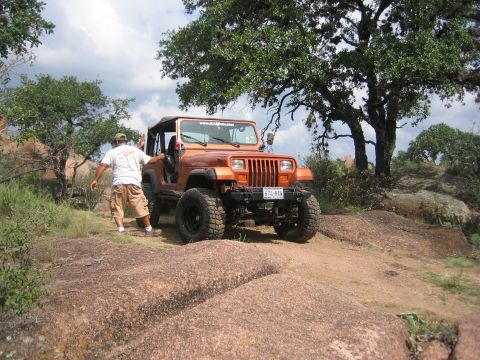 2001 Jeep Wrangler - A man stands next to an orange Jeep Wrangler parked on a rocky, off-road trail under a cloudy sky.