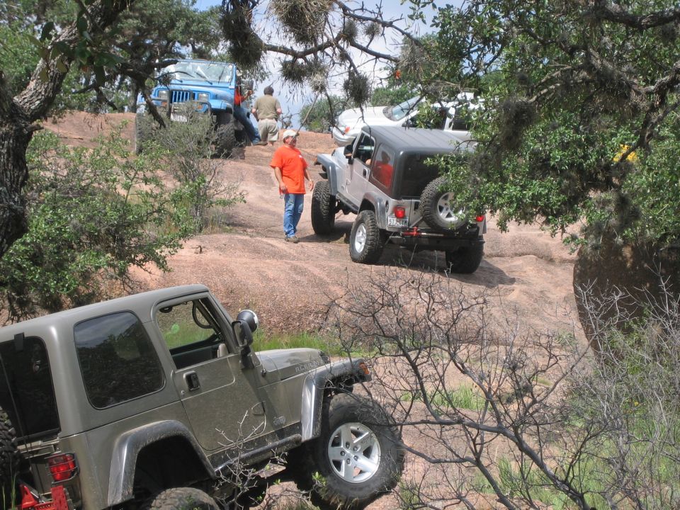 Olive green Jeep Wrangler in foreground, gray Jeep Wrangler on rocky hill, blue Jeep Wrangler behind
