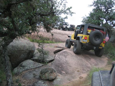 2001 Jeep Wrangler - A yellow 2001 Jeep Wrangler navigates a steep, rocky trail during an off-road event, with several other Jeeps following.