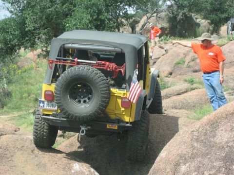 2001 Jeep Wrangler - A yellow 2001 Jeep Wrangler is seen from the rear as it drives over a rocky obstacle course.