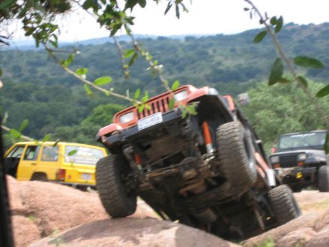 2001 Jeep Wrangler - An orange Jeep Wrangler navigates a rocky trail, with other Jeeps visible in the background.