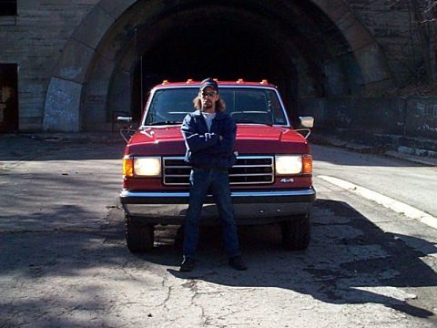 1989 Ford F-150 - A man poses in front of a red Ford F-150 pickup truck, with a tunnel entrance in the background.