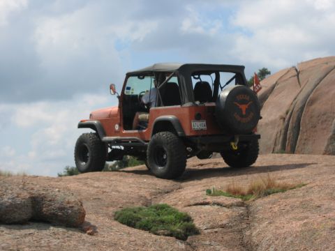 2001 Jeep Wrangler - An orange Jeep Wrangler is parked on a large rock, with a spare tire cover the Texas Longhorns logo.