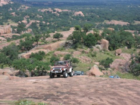 2001 Jeep Wrangler - A 2001 Jeep Wrangler is parked on a rocky hill, with other vehicles and a scenic landscape behind it.