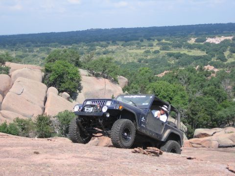 2001 Jeep Wrangler - A dark blue Jeep Wrangler navigates a rocky terrain under a clear sky.