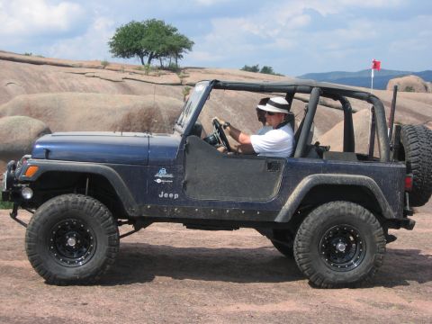 2001 Jeep Wrangler - A blue 2001 Jeep Wrangler is driven by a man wearing a hat through a rocky, outdoor landscape.
