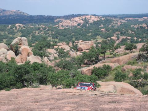 2001 Jeep Wrangler - A red Jeep navigates a , rocky landscape under a partly cloudy sky.