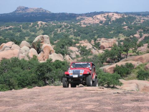 2001 Jeep Wrangler - A red 2001 Jeep Wrangler is parked on a rocky terrain with a mountainous, tree-filled background.