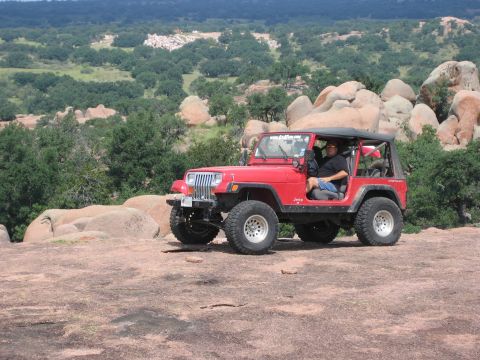 2001 Jeep Wrangler - A red 2001 Jeep Wrangler is parked on a rocky outcrop, with a person inside, enjoying the natural landscape.