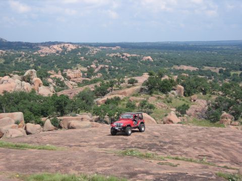 2001 Jeep Wrangler - A red 2001 Jeep Wrangler sits on a rocky outcrop overlooking a vast, green landscape.
