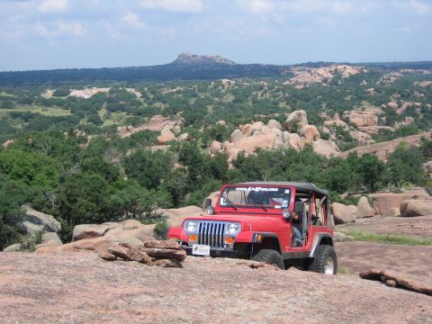 2001 Jeep Wrangler - A red Jeep navigates a rocky landscape under a partly cloudy sky.