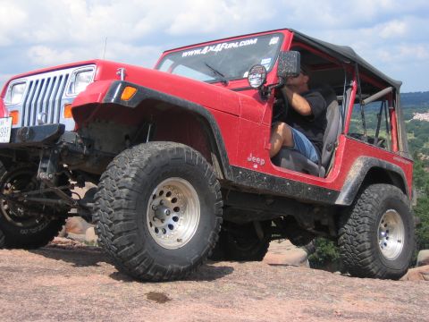 2001 Jeep Wrangler - A red 2001 Jeep Wrangler is shown off-roading on a rocky surface, with a driver visible inside.