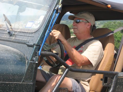 2001 Jeep Wrangler - A man drives a Jeep Wrangler on a sunny day, with trees and hills in the background.