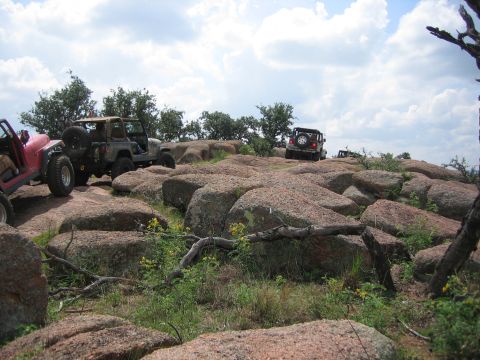 2001 Jeep Wrangler - Several Jeep Wranglers navigate a rocky, off-road trail under a cloudy sky.
