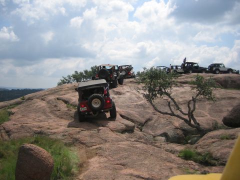 2001 Jeep Wrangler - A convoy of Jeeps navigates a challenging rocky landscape under a partly cloudy sky.