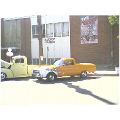 2007 Ford Ranchero - Two pickup trucks are parked in front of a building with a poster on the wall.