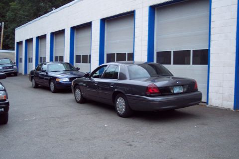 2001 Ford Crown Victoria - Two Ford Crown Victoria police cars are parked outside a building with multiple garage doors.