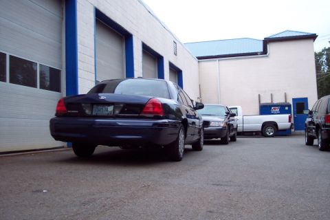 2001 Ford Crown Victoria - A dark blue sedan is parked in front of a commercial building with multiple garage doors.