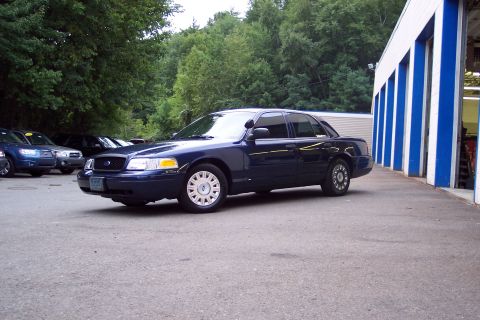 2001 Ford Crown Victoria - A dark blue 2001 Ford Crown Victoria is parked in front of a building with blue and white striped pillars.