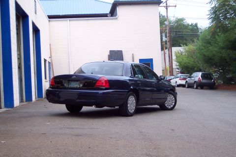 2001 Ford Crown Victoria - A dark blue sedan is parked in an asphalt lot next to a building.