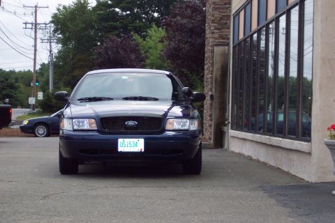 2001 Ford Crown Victoria - A dark blue Ford Crown Victoria is parked in front of a building with large windows. Another vehicle is parked behind it.